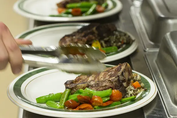 Steak dishes being garnished with vegetables in a restaurant kitchen. 
