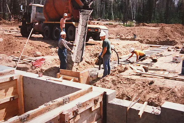 Construction workers pouring concrete at Birchwoods Center building site with a mixer truck.