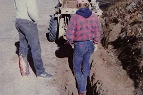 Three men near a backhoe on dirt road adding in a fiber optic line.