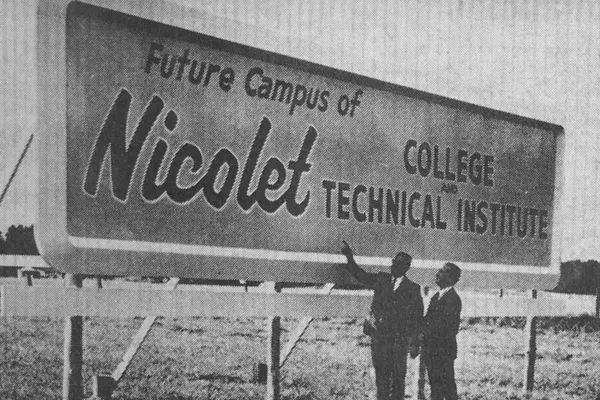 Two men pointing at a large sign for Nicolet College Technical marking the start of the college.