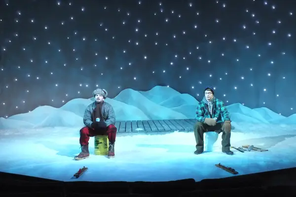 The Nicolet Players performing Almost Maine. Two people sit in snowy landscape under starry sky on stage.