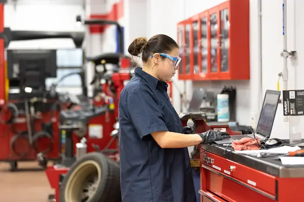 Automotive student on a laptop in a garage with red toolboxes and equipment.