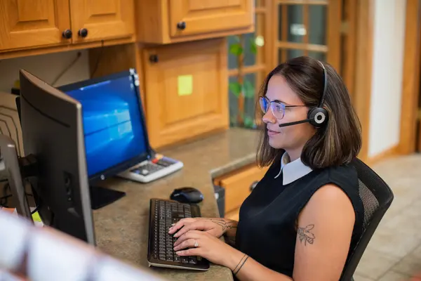 Female student with a headset working at a computer in an office setting.