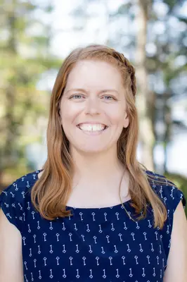Smiling woman with braided hair, wearing a blue shirt, outdoors.