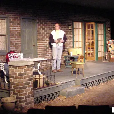 Scene from a Nicolet Players performance with brick-walled stage and two people on a porch.