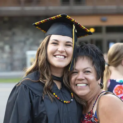 Smiling graduate in cap and gown embracing her proud mother.