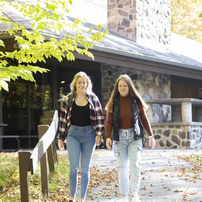 Two female students walking on a leafy path by the Northwoods Center.