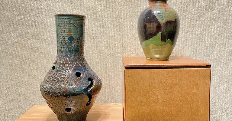 Two decorative vases on wooden pedestals against a textured wall.