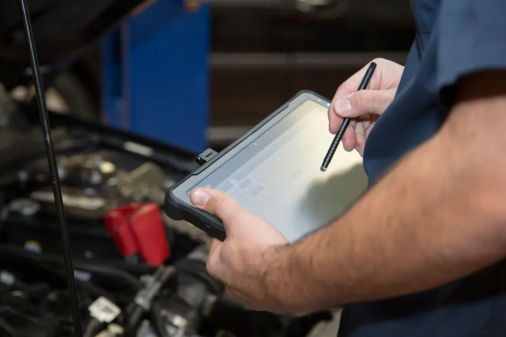 Mechanic using tablet near car engine.