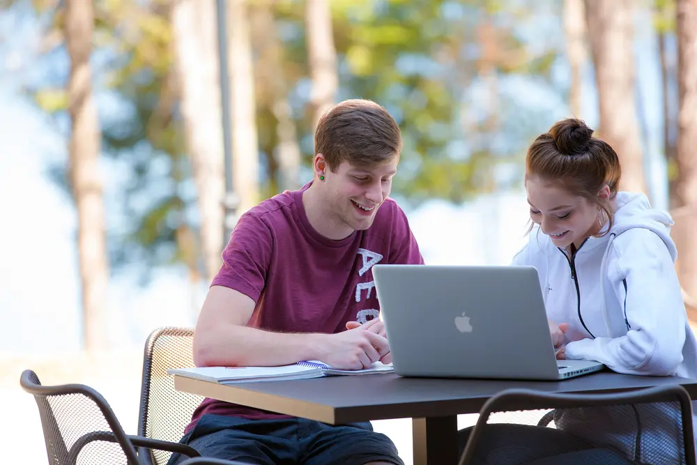 Two students studying together and smiling outside at Nicolet College with a laptop.