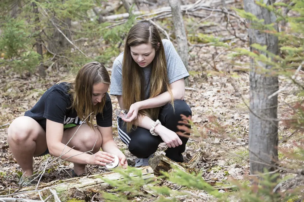 Two female Liberal Arts students collecting samples from forest floor.