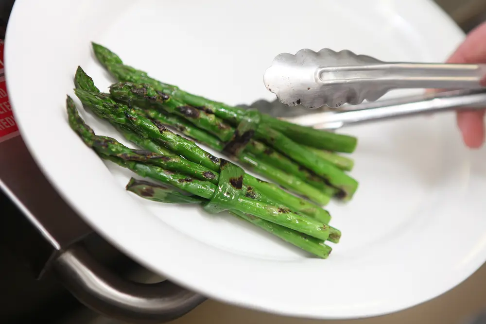 Grilled asparagus being plated with metal tongs.