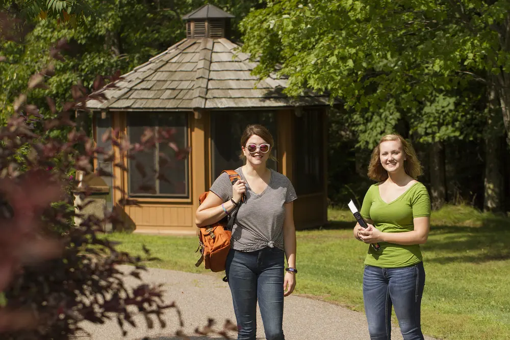 two girls standing outside with books, bags, and sunglasses