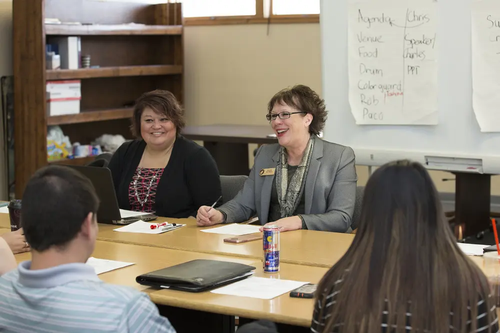 Instructor with student meeting around a table, sharing smiles and notes.