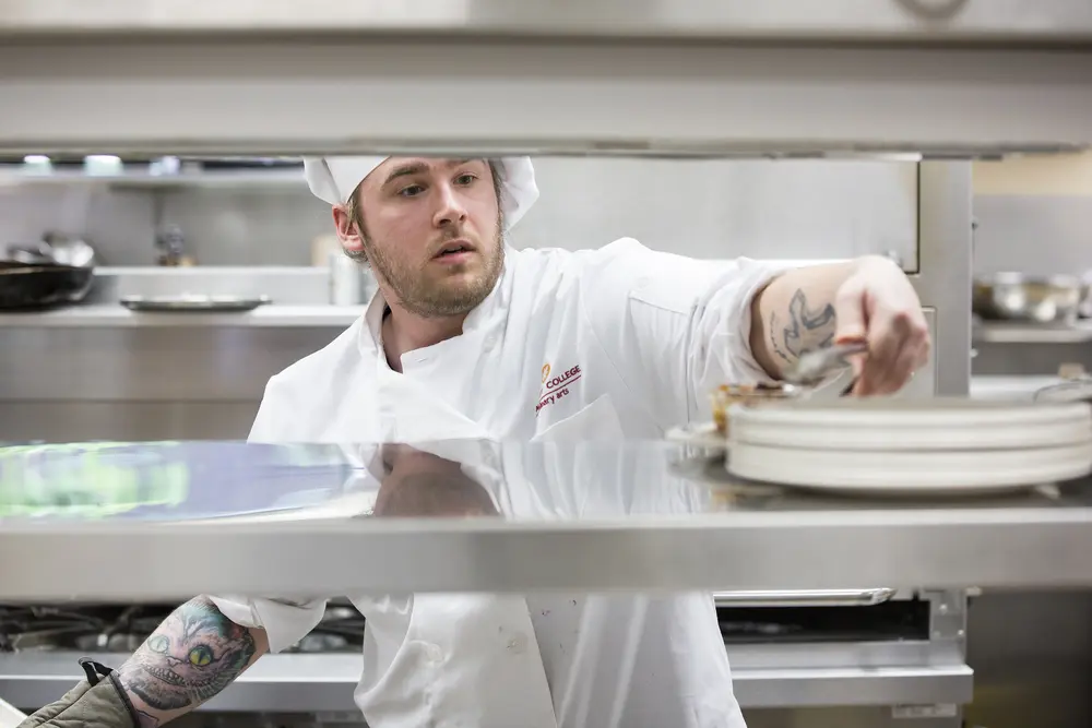 Culinary student plating food in a busy kitchen.