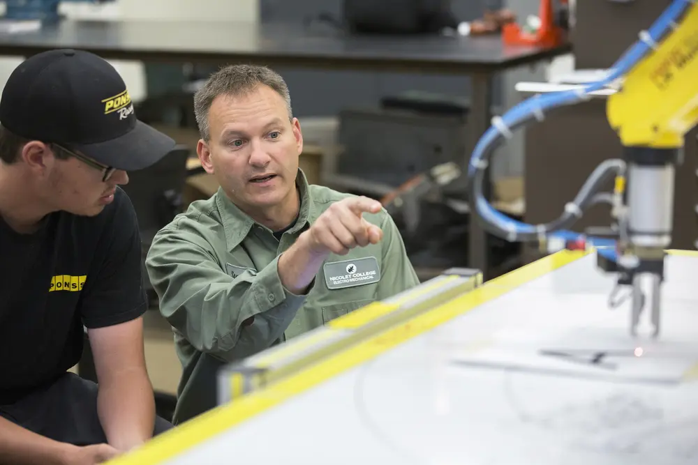 Electromechanical instructor teaching student and pointing at a machine.