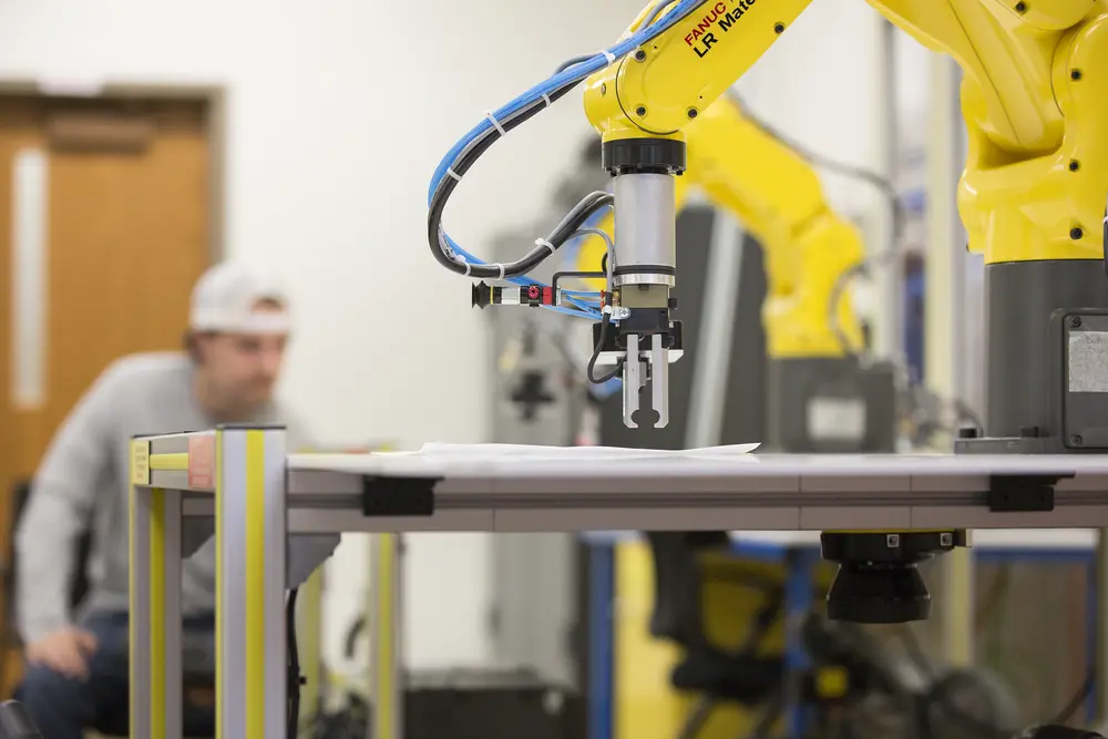 Yellow robotic arm working on a table, person blurred in the background.