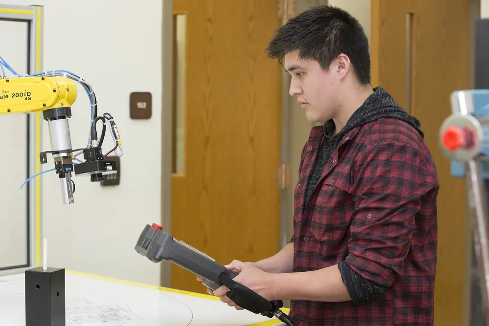Electromechanical student operating robotic arm with a controller.