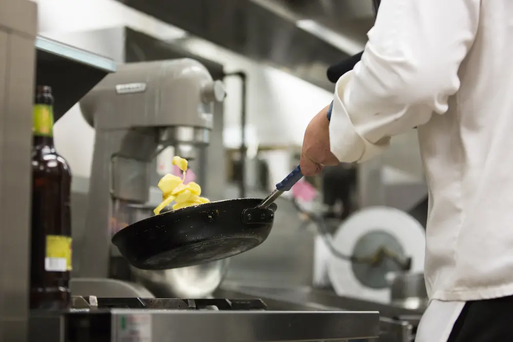 Culinary student flambéing apples in a frying pan in a commercial kitchen.