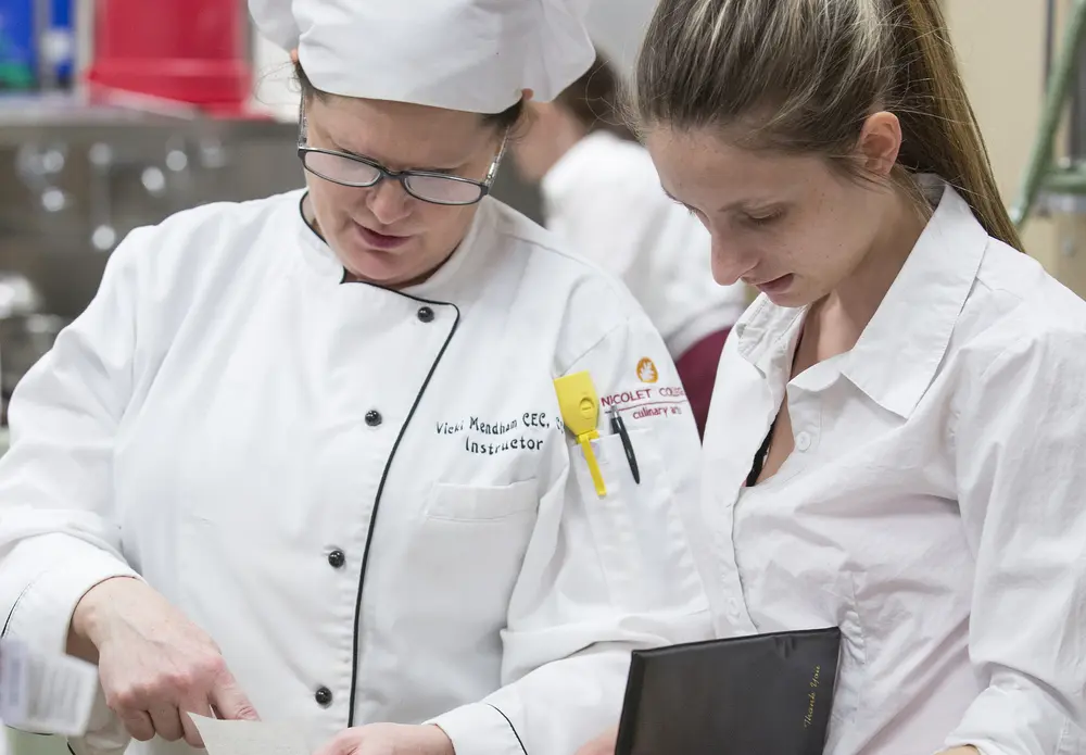 Culinary instructor conversing with culinary student in a kitchen.