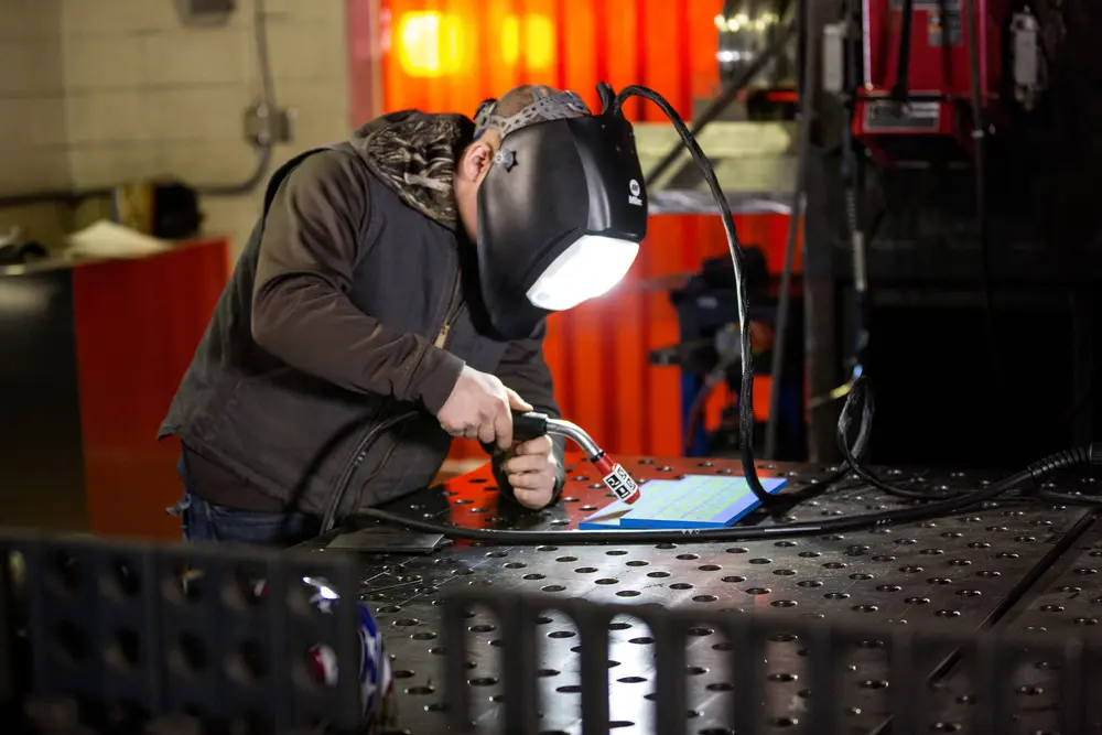Welding student in protective gear using a virtual welder simulator.
