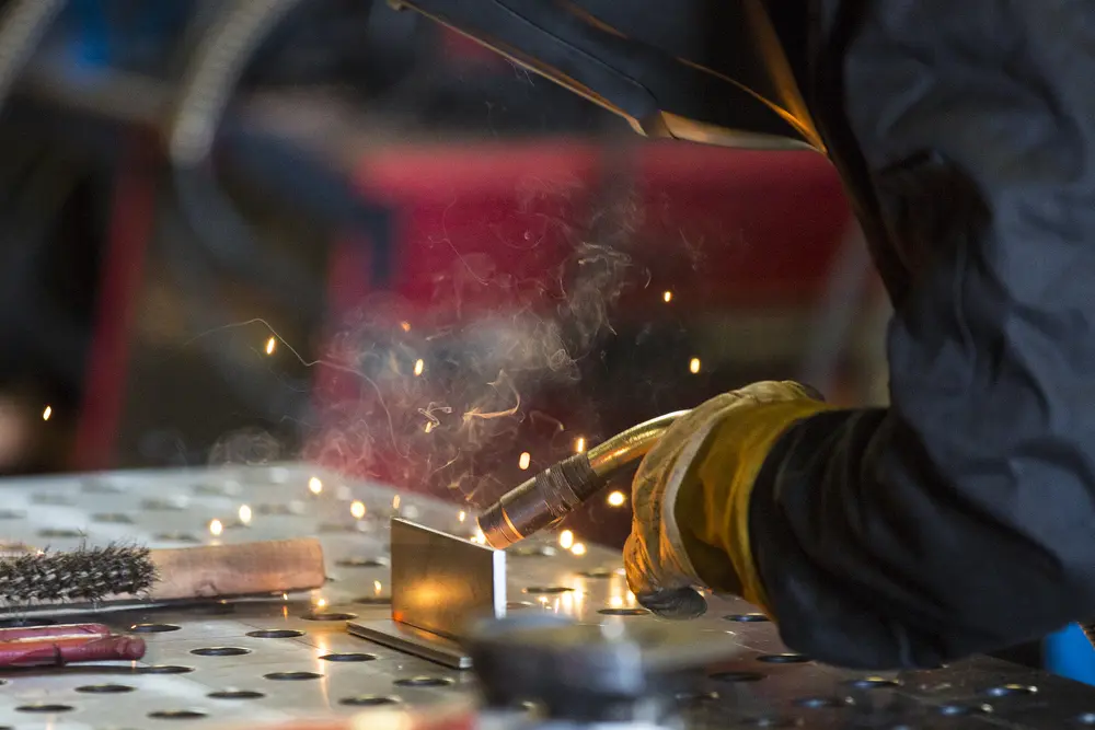 Welding sparks fly as a gloved hand works on metal.