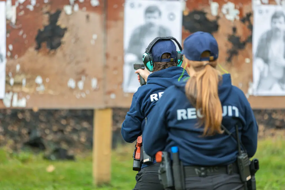 Two recruit academy students aiming at paper targets on a shooting range.