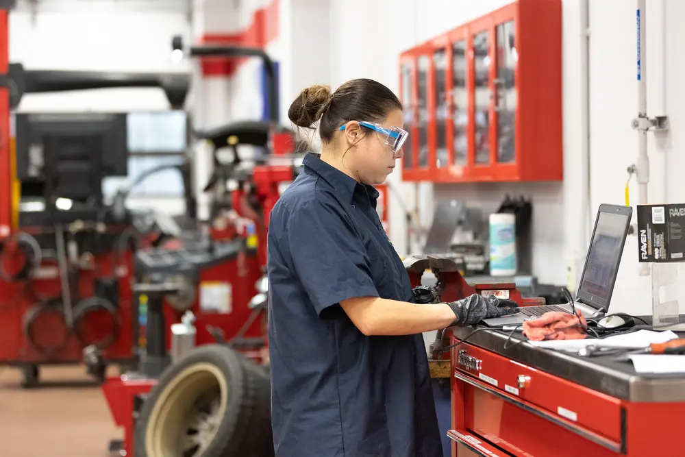 Automotive student on a laptop in a garage with red toolboxes and equipment.