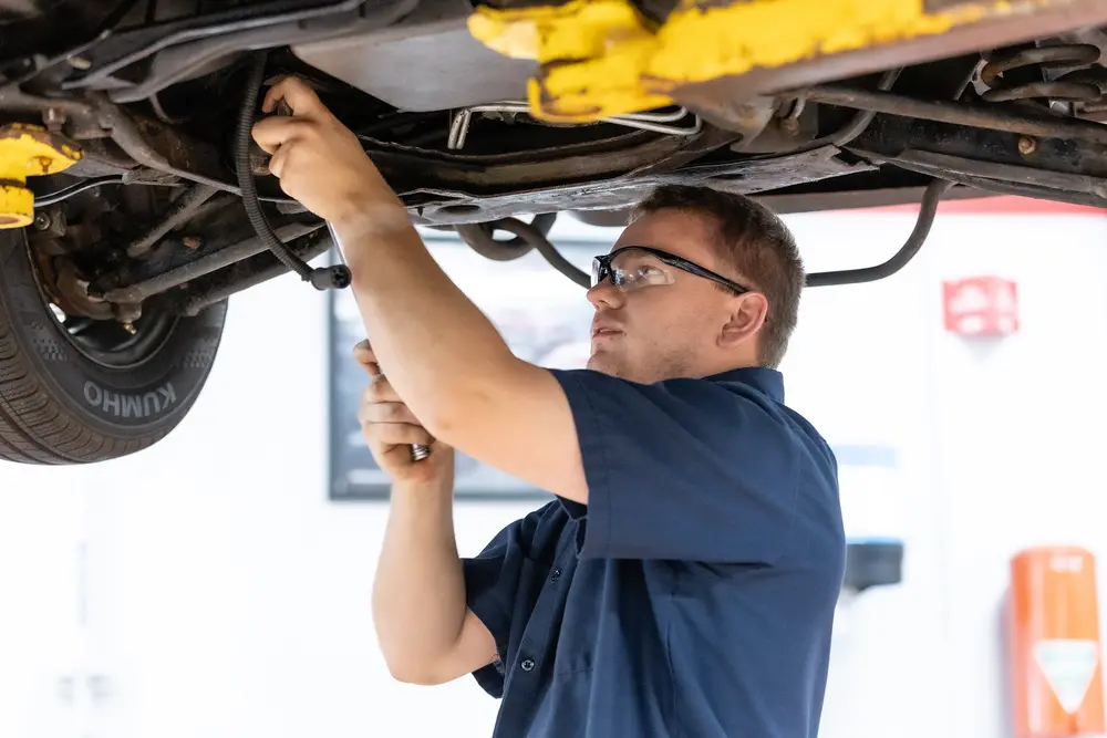 Mechanic working under a car, wearing safety glasses.