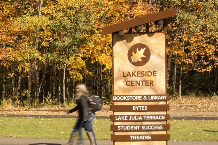 Sign reading "Lakeside Center" with autumn trees and a person walking in the background.