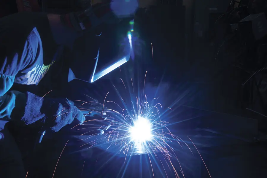Welder in helmet, sparks flying in dark workshop.