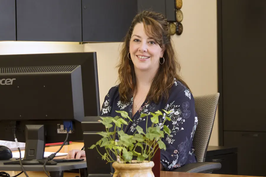 Female administrative professional smiling at a desk with a computer.
