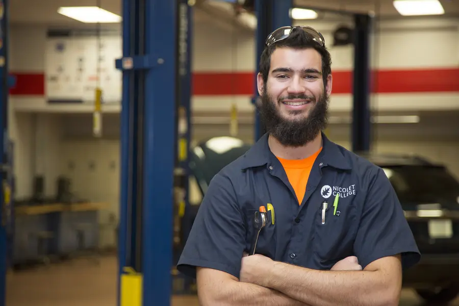 Automotive student smiling in a workshop with cars in the background.