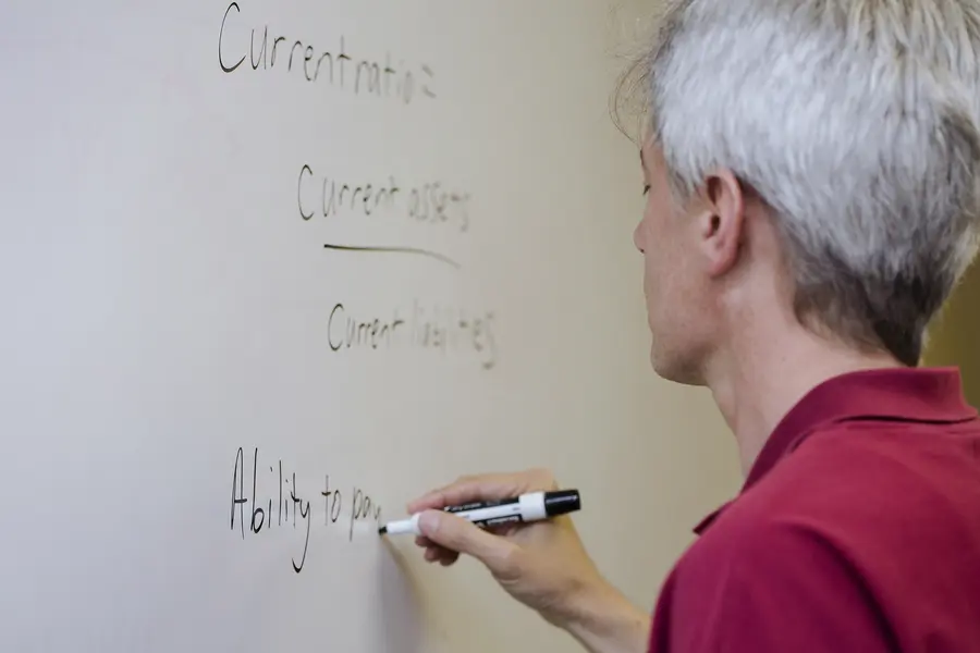 Male instructor in red shirt writing on a whiteboard.