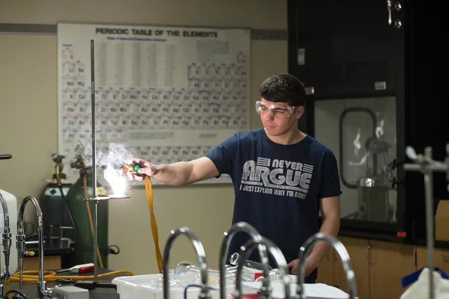 Student conducting science experiment with a Bunsen burner in a lab classroom.