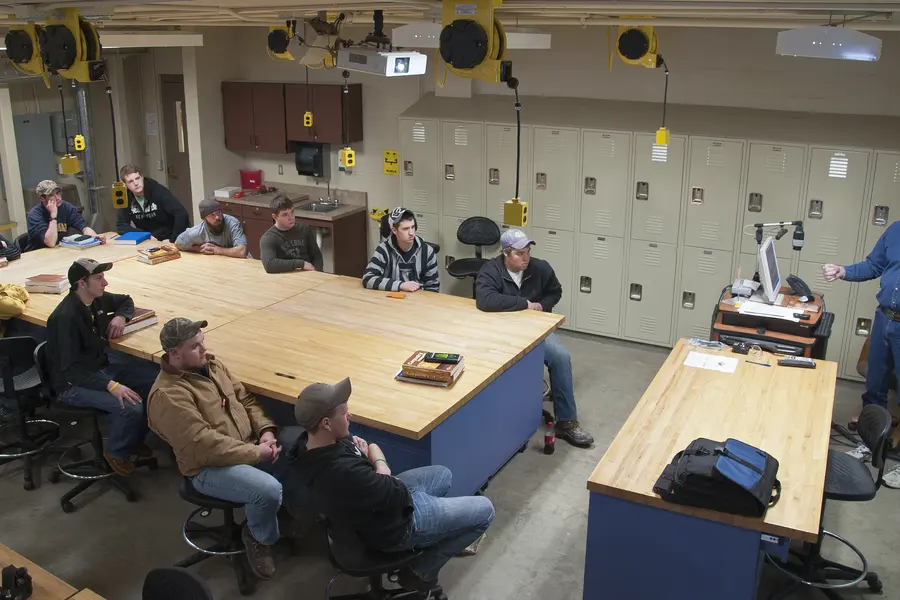 Classroom with apprenticeship students seated around a table, instructor speaking at the front.