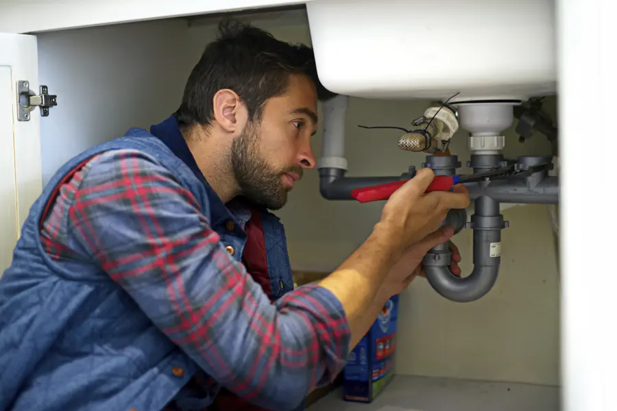 Male plumbing apprentice fixing a sink pipe.