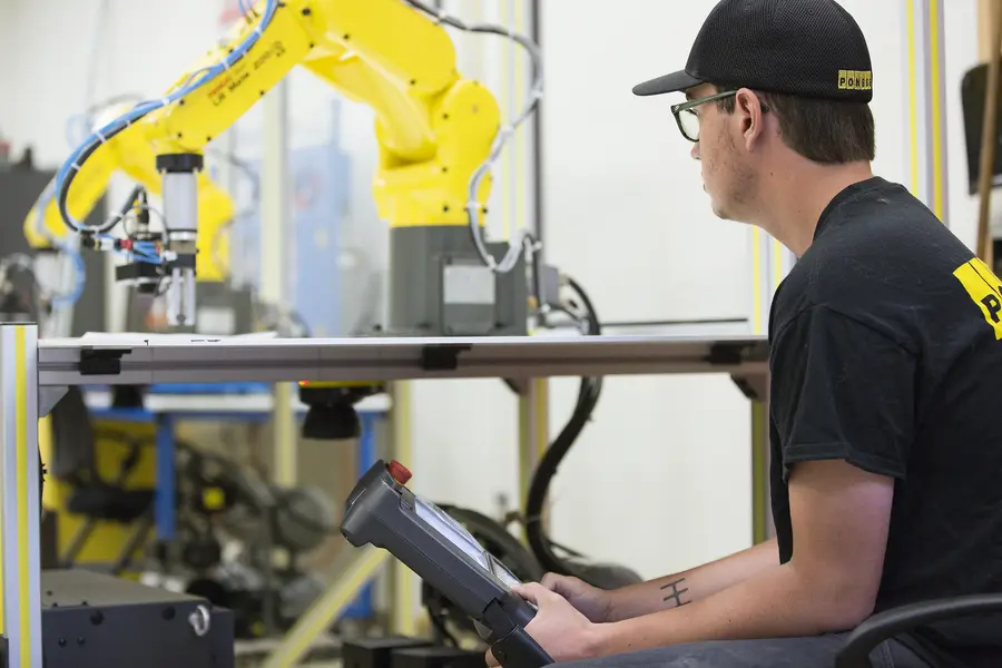Electromechanical student operating a yellow robotic arm with control panel.