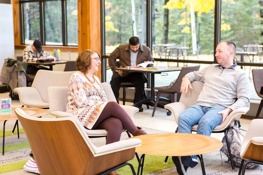 Cozy lounge with people chatting and studying, large windows in the background.