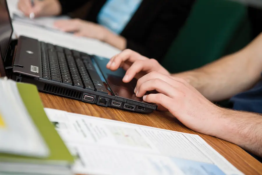 Hands typing on a laptop next to documents on a table.