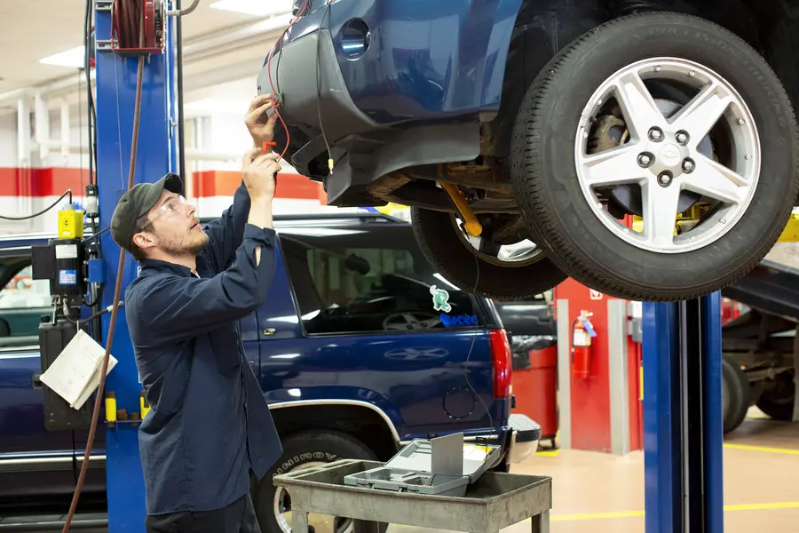 Automotive student working on a car lifted in an auto repair shop.