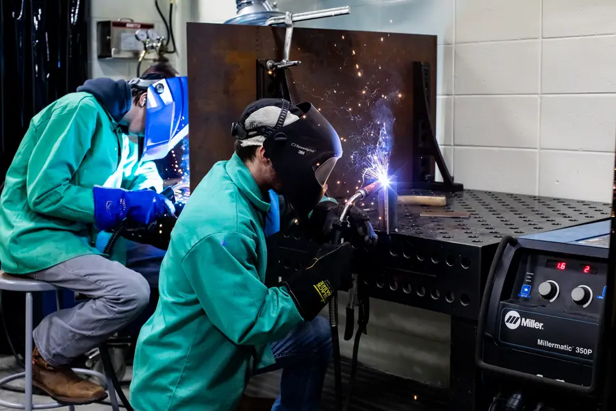 Two welding students in a workshop, wearing protective gear.