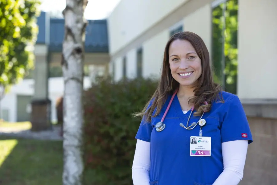 Alumni Dani Lilek smiling outside, wearing blue scrubs and an Aspirus name badge.