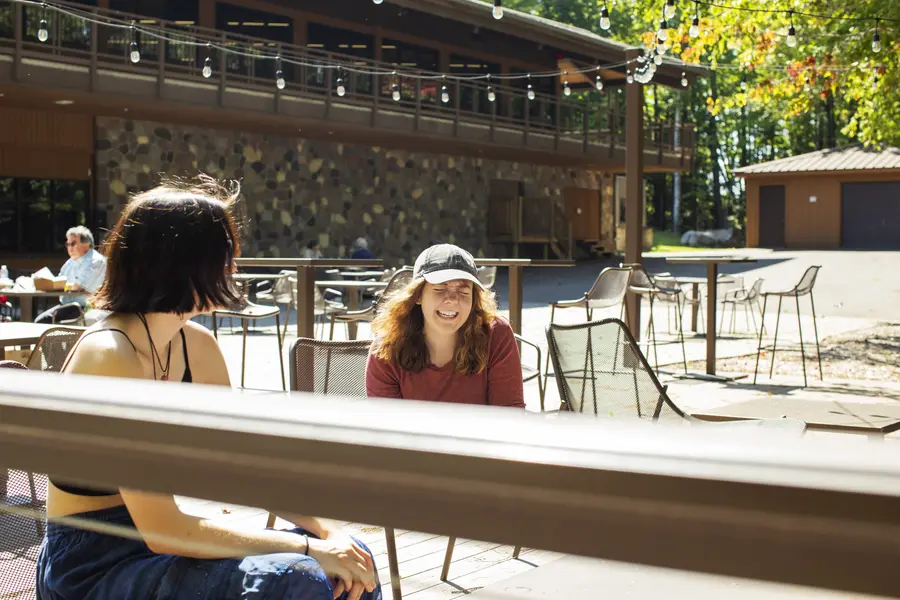 Two students smiling and talking on a sunny outdoor patio.