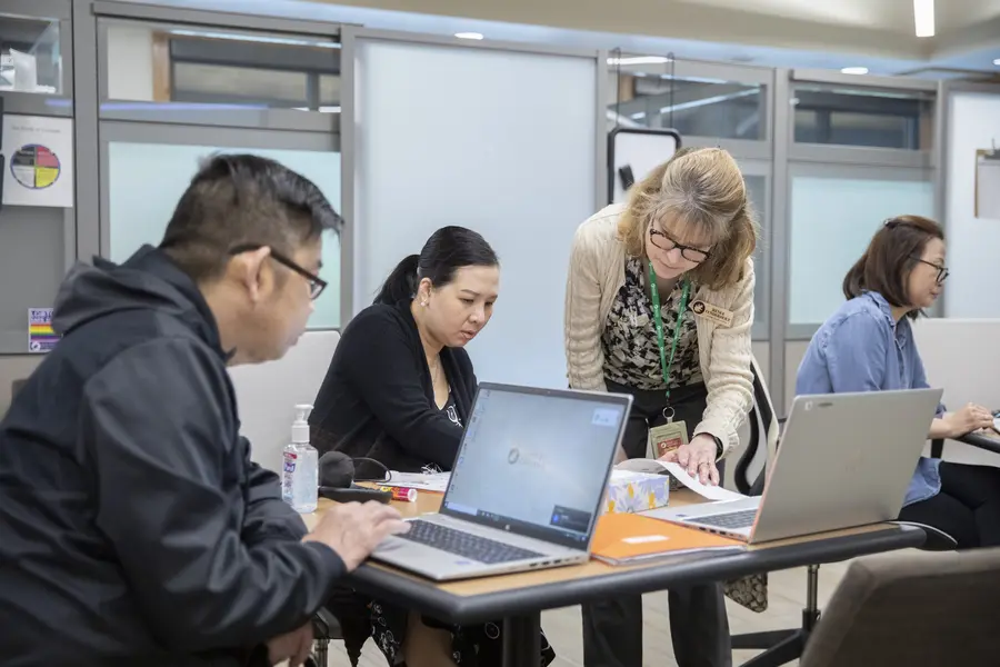 Students working on laptops receiving help from an Academic Success instructor in an office setting.
