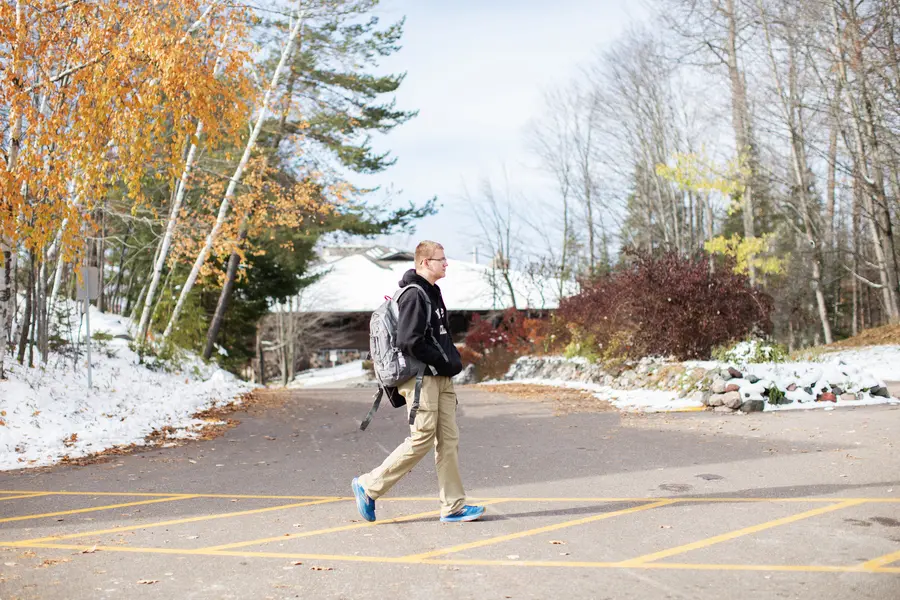 Student walking outside, autumn trees, patches of snow on the ground.