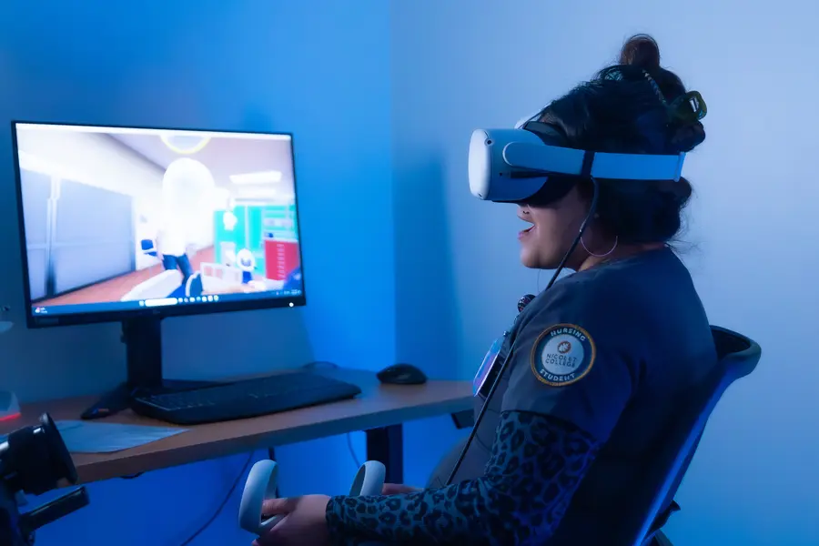 Female nursing student using VR headset in a dimly lit room with a computer screen.