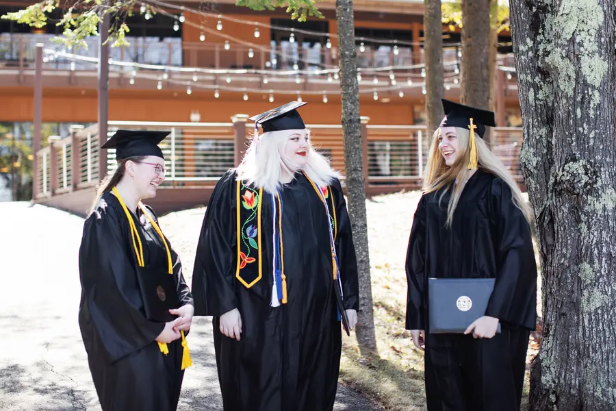 Three graduates in caps and gowns, smiling and talking outdoors.