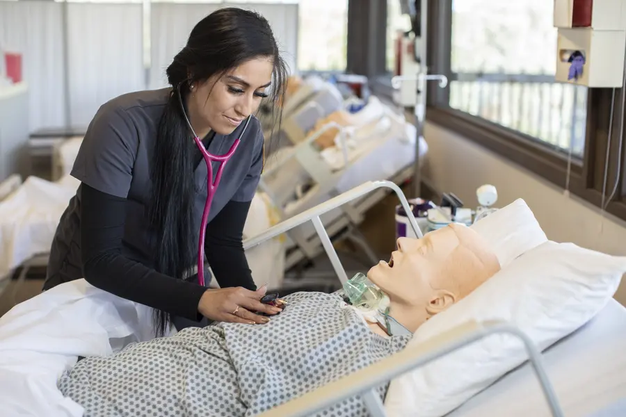 Nurse practicing on a medical manikin in a hospital room.