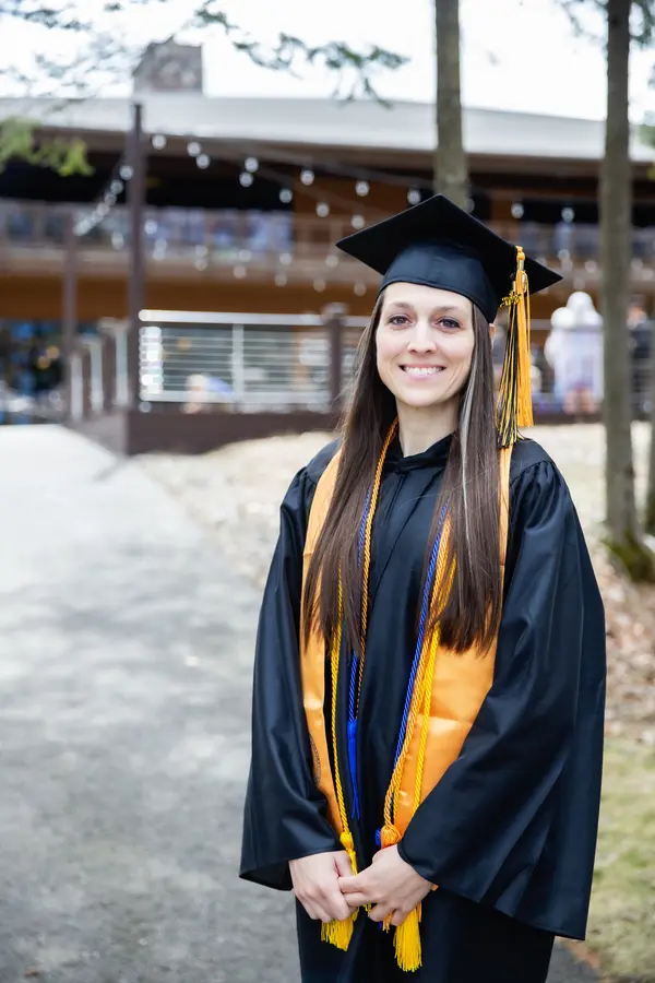 Graduating female student in cap and gown smiling outdoors.